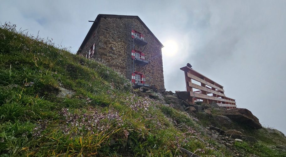 Breslauer Hütte Ein Steinhaus auf einer Wiese, umgeben von grüner Vegetation und teilweise bewölkten Himmel.