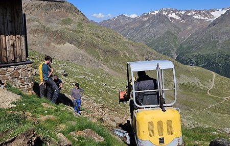 Breslauer Hütte Arbeitsteam Bauarbeiter mit Bagger in bergiger Landschaft, neben ihnen stehen weitere Personen.